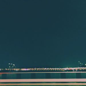 Illuminated city by sea against clear sky at night