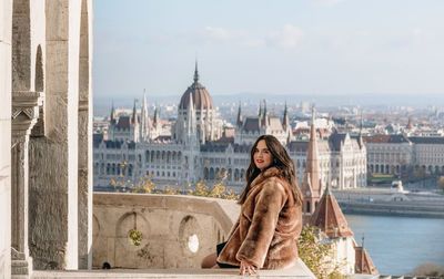 Portrait of beautiful young woman on balcony overlooking hungarian parliament in budapest, hungary