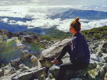 Woman sitting on mountain against sky