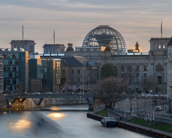 View of cityscape against river during sunset