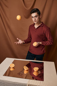 Man tossing oranges against brown background