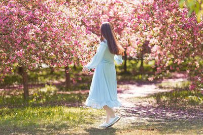 Happy brunette girl in blue dress, is dancing in a pink blooming garden