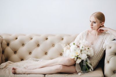 Young woman holding flowers while resting on sofa