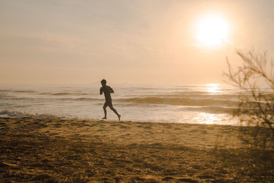 Silhouette man run on beach with sunrise and sea background