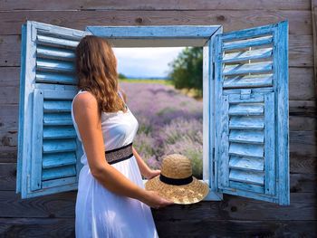 Woman in white dress looking out the open window at a field of lavender flowers