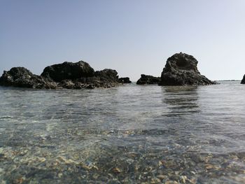 Rocks in sea against clear blue sky