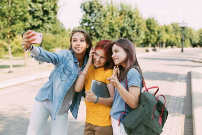 Three charming friends take selfies with their phone on the way to school. the concept of friendship