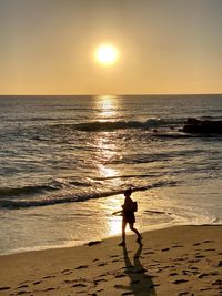 Silhouette woman on beach against sky during sunset