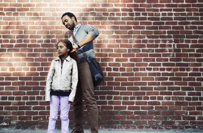 Father tying daughter's hair while standing against brick wall