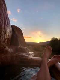 Low section of person by sea against sky during sunset