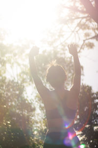 Rear view of woman with arms raised standing against sky