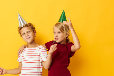 Portrait of sibling wearing party hat against yellow background