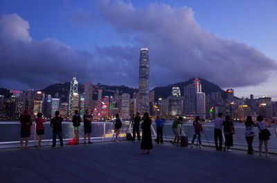 People on illuminated buildings in city against sky