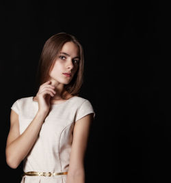 Portrait of beautiful young woman standing against black background