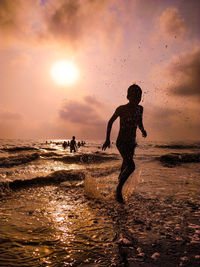 Silhouette boy on beach against sky during sunset