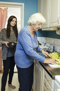 Young woman looking at grandmother preparing food in kitchen