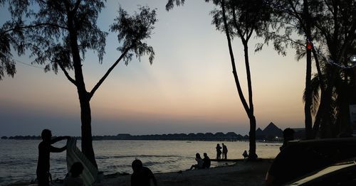 Silhouette people on beach against sky during sunset