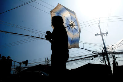 Silhouette person with umbrella against clear blue sky