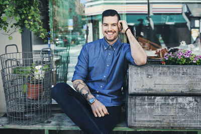 Portrait of confident male owner leaning on crate outside plant shop