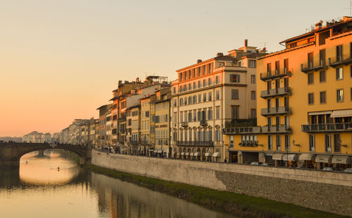 Bridge over river by buildings against sky during sunset