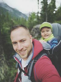 Portrait of smiling father carrying son in stroller in forest