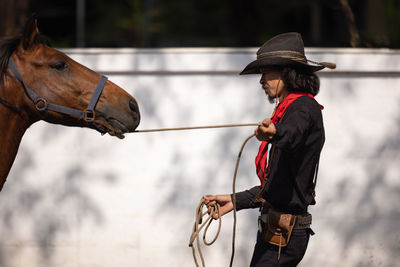 In an outdoor barn, one man dressed as a cowboy trains his horse to run in a circle around him.