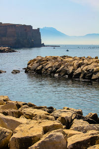 Rocks on shore by sea against sky