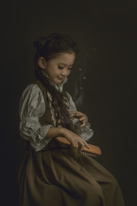 Girl combing hair while sitting against black background