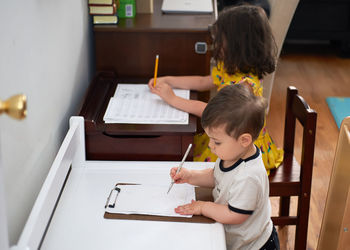 Little toddler copying his sister doing her homework