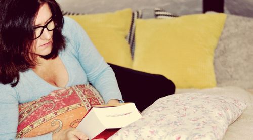 Woman holding book while reclining on bed at home