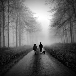 Rear view of people walking on dirt road in winter