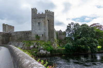 Old building by river against cloudy sky