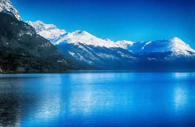 Scenic view of lake and snowcapped mountains against blue sky