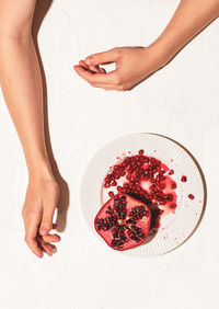 The woman's hands are lying on a white table next to a plate with a sliced juicy pomegranate.