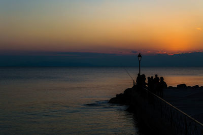 Silhouette people on pier by sea against sky during sunset