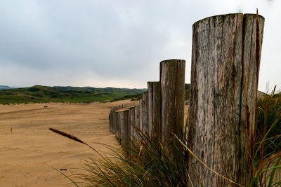 Wooden fence on field against sky and dune