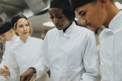 Female and male trainee working by teacher guiding at culinary school