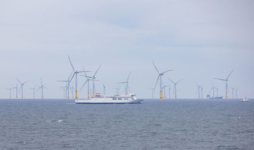 Ship and turbines in sea against sky