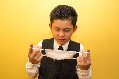 Portrait of boy holding camera against yellow background