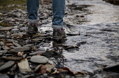 Low section of person standing on pebbles in river in rainy season