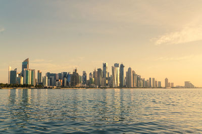 Sea by modern buildings in city against sky