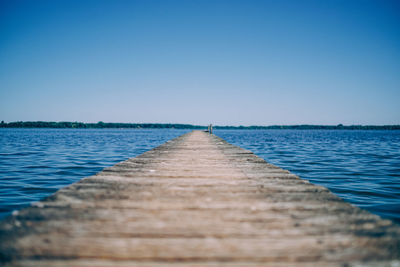 Surface level of pier over lake against clear blue sky