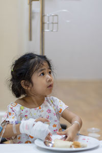 Cute girl with bandage having food at table in hospital