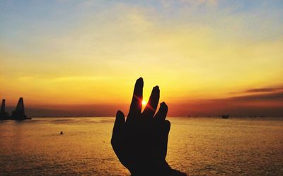 Silhouette hand against sea during sunset