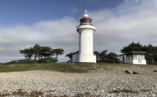 Lighthouse on field by building against sky