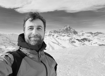 Portrait of young man with snowcapped mountains against sky