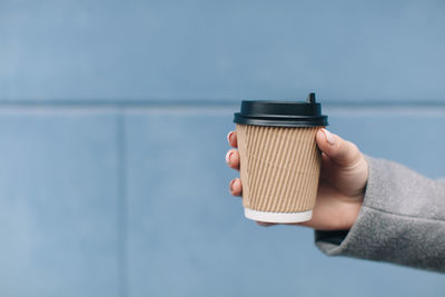 Cropped hand of woman holding disposable cup against wall
