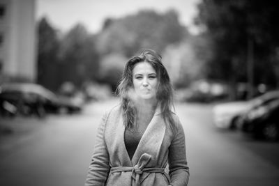 Portrait of woman exhaling smoke while standing on street in city