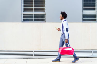 Fashionable man with bag walking by wall