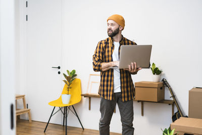 Happy mature man in a newly rented ore purchased apartment using a laptop.